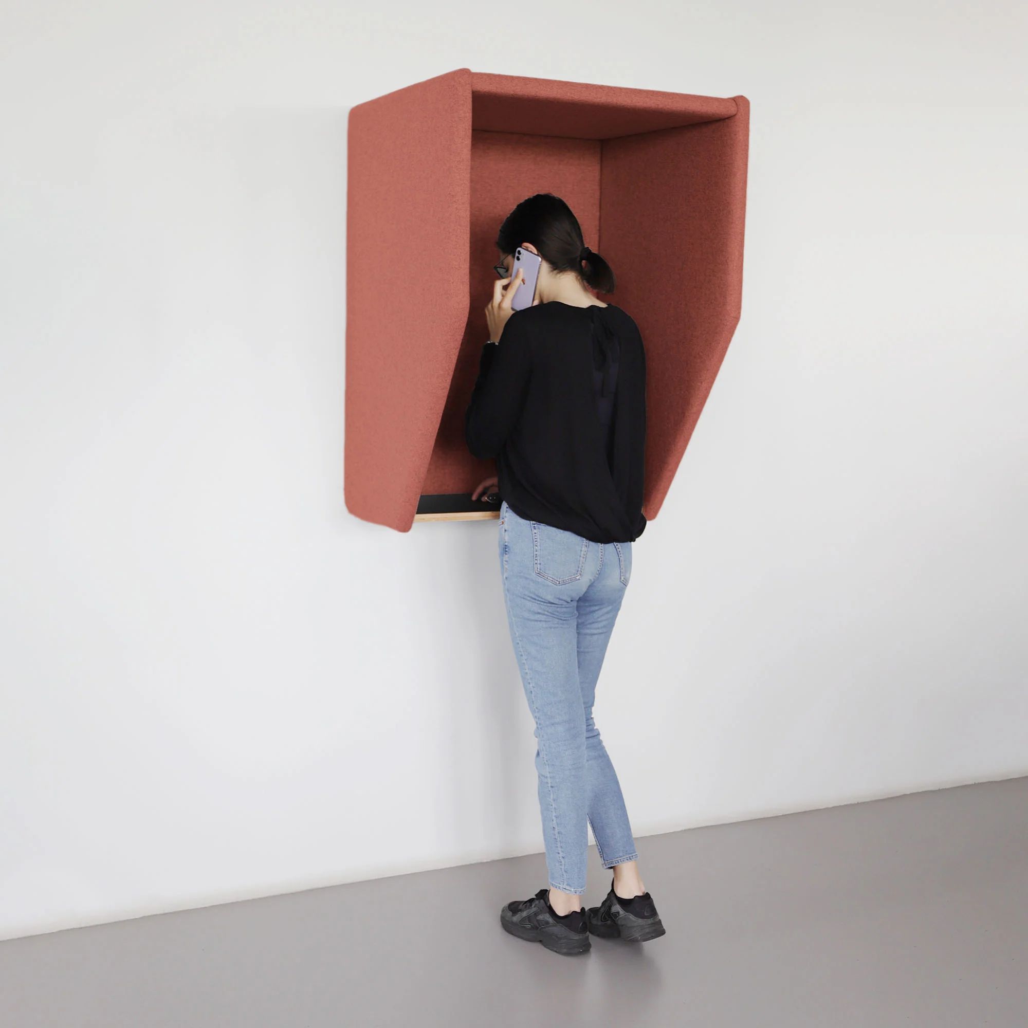 Person using a coral acoustic phone hood mounted on a wall