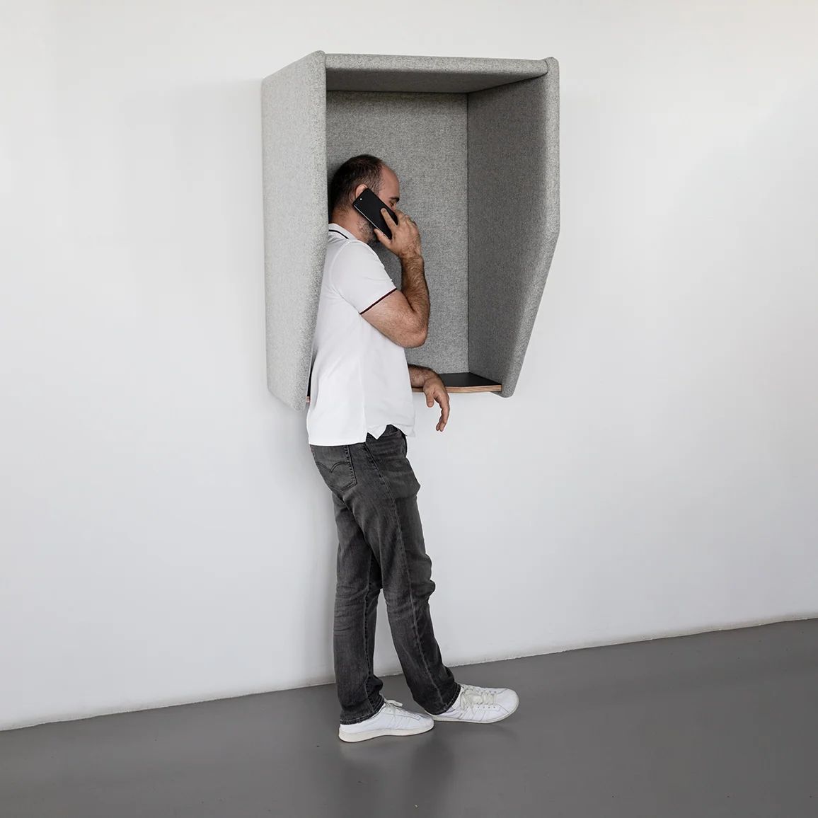 Person using a grey wall-mounted acoustic phone hood