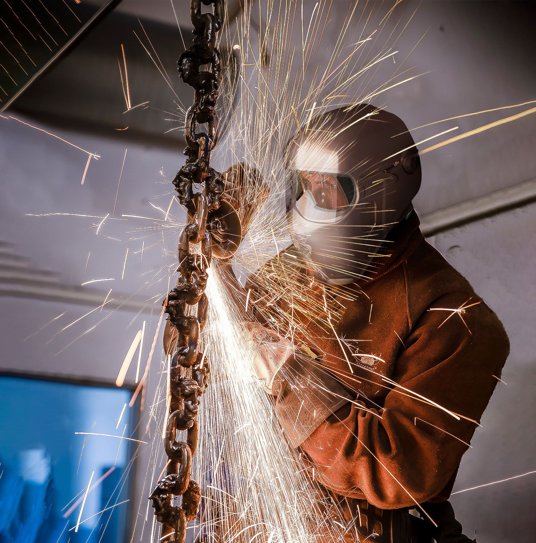 Welder wearing the WeldLite helmet while grinding metal amid a field of sparks